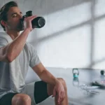 Exhausted man drinking water from sports bottle after fitness training in gym