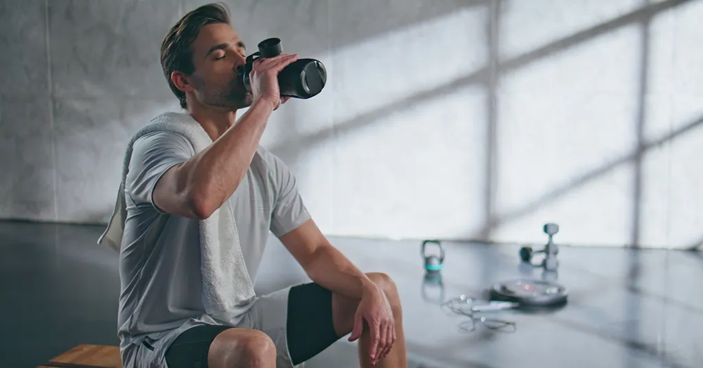 Exhausted man drinking water from sports bottle after fitness training in gym