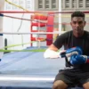 Young male boxer putting on gloves while sitting on boxing ring