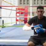 Young male boxer putting on gloves while sitting on boxing ring